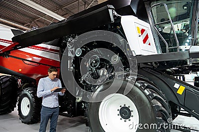 Serviceman with digital tablet on a next to ombine harvester with open hood.. Stock Photo