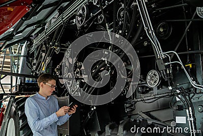 Serviceman with digital tablet on a next to ombine harvester with open hood.. Stock Photo