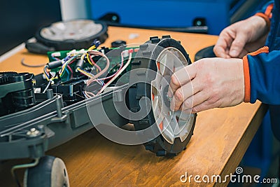 Serviceman replacing wheels on robotic lawnmower, motorized lawnmower being serviced on a table after a year of use in the mud Stock Photo