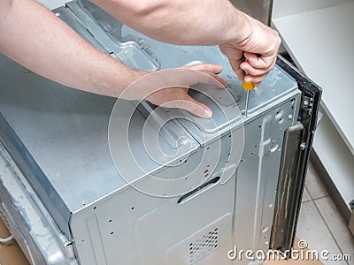 Serviceman unscewing top cover of broken electric oven Stock Photo