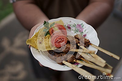 A serving of Balinese fish satay topped with fresh tomatoes, celery and crispy chips. Presented by hand by the waiter. Looks Stock Photo