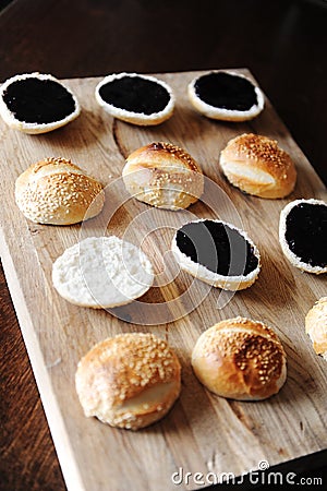 Sesame burgers buns split in half on wooden cutting board. Dark berry sauce on top. Cooking process Stock Photo