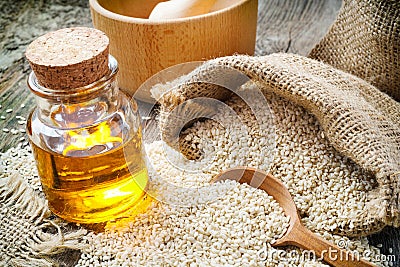 Sesame seeds in sack and bottle of oil on rustic table Stock Photo