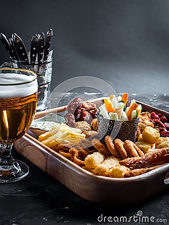 Set of assorted beer snacks - sausages, chicken wings, croutons, onion rings and squid rings on wooden board with sauce and glass Stock Photo