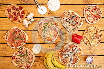 set of assorted small pizzas on wooden table. Kiwis, mushrooms, goat cheese roll, ripe bananas, peppers Stock Photo