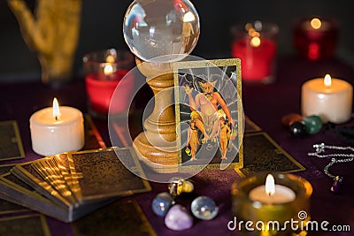 Burning colorful candles with devil tarot cards and stones on table Stock Photo