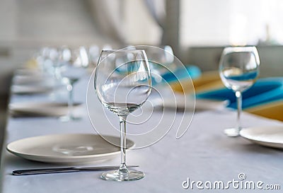 Set of clean empty wine glasses and plates on a dining table with colorful chairs on a restaurant interior pastel background. A cl Stock Photo