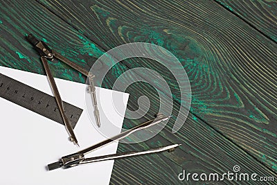 Set for drawing. Two compasses, a metal ruler and a sheet of white paper. They lie on pine boards painted in black and green Stock Photo