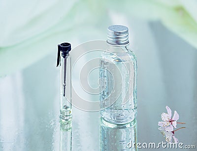 A set of glass flasks and blurred tender pink flower on the right, placed on wet reflecting surface. Stock Photo