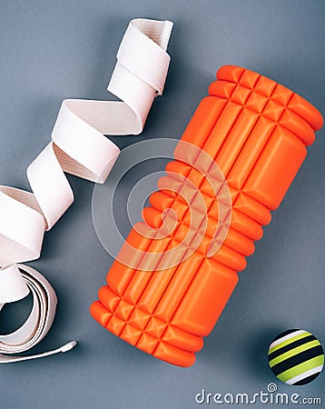 Set of green fascia release ball, orange bumpy foam massage roller for trigger points and belt over grey background. Stock Photo