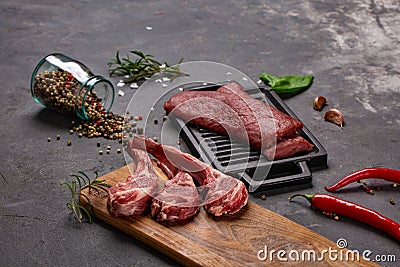 Set of Raw uncooked black angus beef tomahawk steaks on bones and veal tenderloin served with chilli and peppercorns. Rustic style Stock Photo