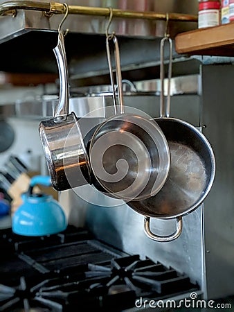 Set of sauce pans hanging to the right of a stove top in a nice kitchen with a stainless steel backsplash and a tea kettle Stock Photo