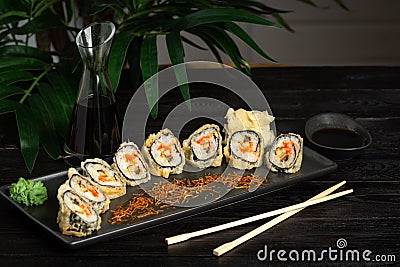 set of sushi rolls on a black plate on a black wooden background with green leaves of a houseplant Stock Photo