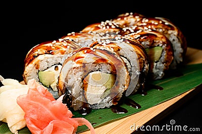 Set of sushi rolls dragon served on wooden board with plant leaves, pickled ginger and wasabi on black background. Stock Photo