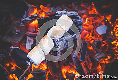 Set of sweet marshmallows roasting over red fire flames. Marshmallow on skewers roasted on charcoals Stock Photo