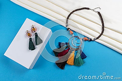 Set of tassel earrings and wood beads with colorful tassels and crystal beads necklace boho style on white scarf and blue paper Stock Photo