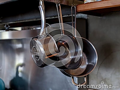 Set of three sauce pans hanging in a nice kitchen with a stainless steel backsplash and a tea kettle Stock Photo