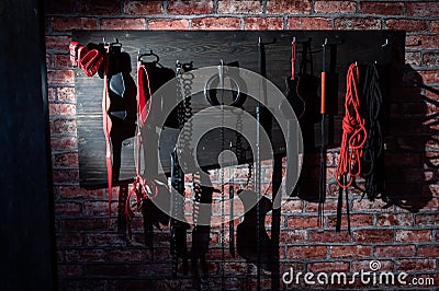 A set of varied leather lashes for sexual pleasures hang on a wooden hanger on a brick wall. Sex equipment in red and Stock Photo