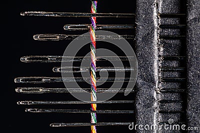 A set of various sized dusty steel sewing needles with a single twisted multi-colored thread woven through them Stock Photo