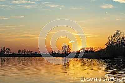 The setting sun is barely visible through the trees along the lake Zoetermeerse Plas, Zoetermeer, Netherlands Stock Photo