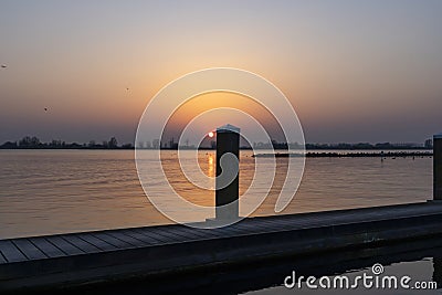 The setting sun almost disappears behind one of the bollards of a landing stage at Lake Zoetermeerse Plas in Zoetermeer, The Nethe Stock Photo