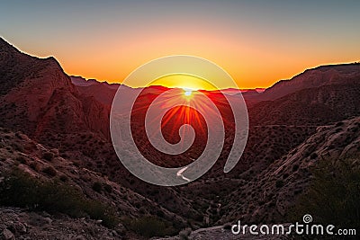 setting sun, fiery canyon and silhouette of mountain range in the background Stock Photo