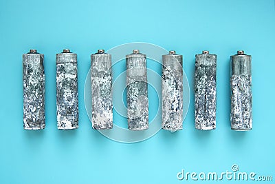 Seven heavily oxidized AA batteries unwrapped and laid out in a row on a blue background Stock Photo