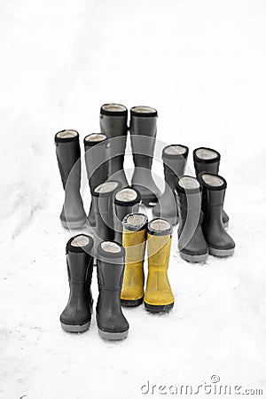 Seven pair of winter boots different sizes standing on snow, one pair is yellow. Seasonal shoes for all family, adult and child Stock Photo