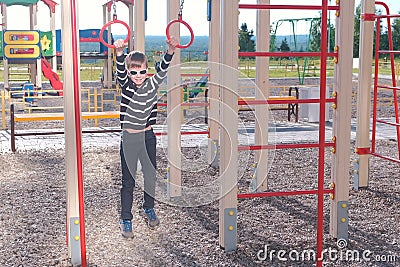 Seven-year-old boy hangs on the gymnastic rings on the Playground. Stock Photo