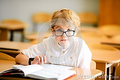Seven years old child with glasses writing his homework at school. Boy studing at table on class background Stock Photo