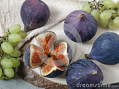 Several berries of figs and small bunches of grapes lie on a table on a circle of natural sawn wood and a linen napkin. Stock Photo