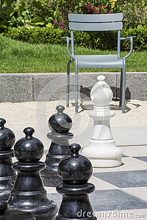 Several black chessmen and white bishop on the street chessboard with chair Stock Photo