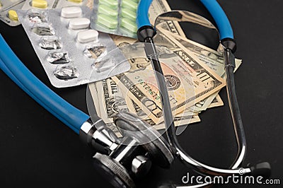 Several blisters with different tablets, a stethoscope, and dollar bills on a black background. Only together will we stop the Stock Photo