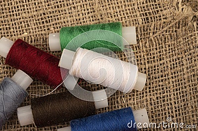 Several coils of multicolored sewing thread against a background of coarse-textured burlap. Close up Stock Photo