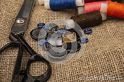 Several colored buttons of different sizes, reels of colored sewing thread, and large vintage sartorial scissors against a Stock Photo