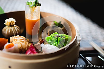 Several different traditional Chinese dimsum dumplings in a wooden basket cooked for guests on a wooden table in a Stock Photo