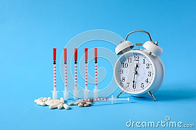 Several insulin syringes next to an alarm clock on a blue background. Stock Photo