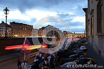 Several motorbikes parked in a row along the street with light trails of a car and cityscape of Florence Stock Photo