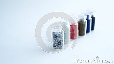 Several small cans with colored beads for manicure stand in a row on a white background. Stock Photo