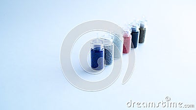 Several small cans with colored beads for manicure stand in a row on a white background. Stock Photo