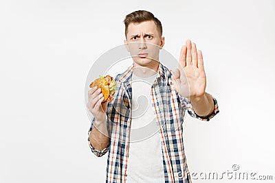 Severe young man holding burger, showing stop gesture with palm isolated on white background. Proper nutrition or Stock Photo