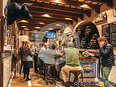 Crowd of people having dinner inside tapas bar with bull head and old wine barrels Editorial Stock Photo