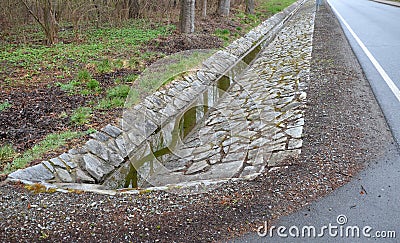 Sewer pipes under the bridge. crossing the ditch by the road. concrete hole with stone paving surroundings. The gutter drains arou Stock Photo
