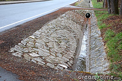 Sewer pipes under the bridge. crossing the ditch by the road. concrete hole with stone paving surroundings. The gutter drains arou Stock Photo