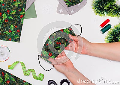 Sewing Christmas Face Mask with Holly Pattern flat lay. Top view Taylor hands . DIY and Handmade Stock Photo