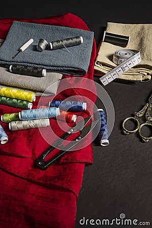 Sewing objects with vintage golden metal scissors, various needles, thimbles, red cloth, spools of colored threads, cloth, Stock Photo