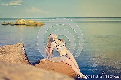 Sexi blond female sunbathing on rock by sea Stock Photo