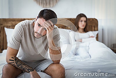 Sexual dysfunction. Husband holds his head, upset wife on bed Stock Photo