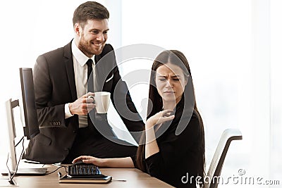 Sexual harassment at work. Male businessman sits and flirts with annoyed female assistant at workplace showing Stock Photo