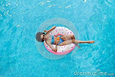 Sexy African American woman with summer drink relaxing on inflatable ring at swimming pool, overhead view Stock Photo